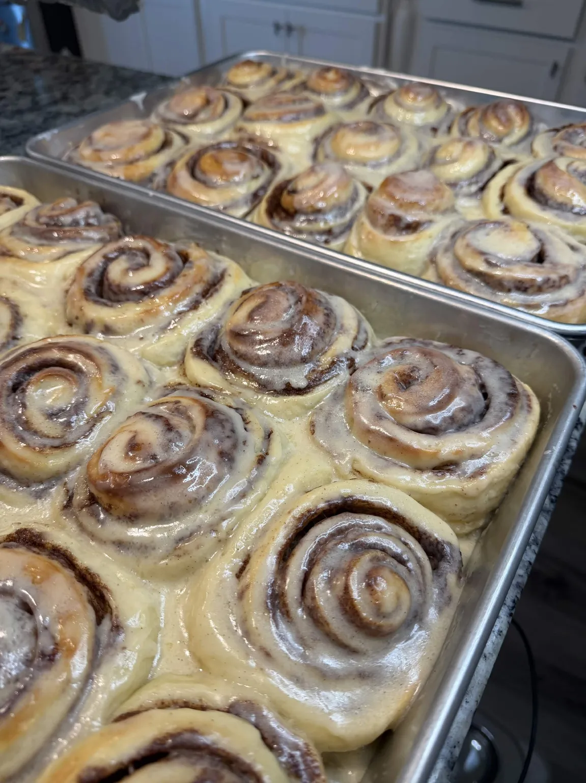 Trays of Rolling Dough Co cinnamon rolls with icing in our kitchen